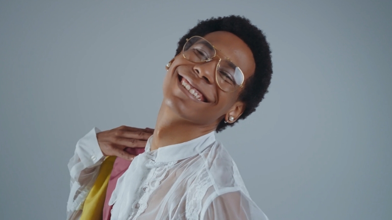 A person smiling and posing confidently, wearing a white shirt and glasses