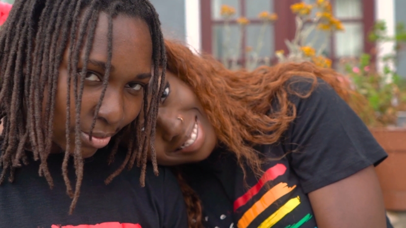 The image shows two people smiling and leaning against each other, wearing matching t-shirts