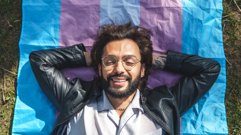 A person lying on a transgender pride flag, smiling and enjoying the moment