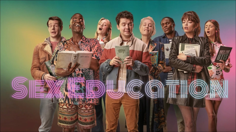 Cast of Sex Education stands together holding books against a colorful background
