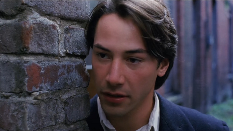 A man leans against a brick wall, lost in thought, in a scene from My Own Private Idaho
