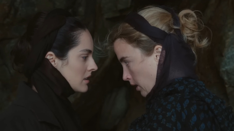 Two women share an intense gaze in a dimly lit scene from Portrait of a Lady on Fire (2019)