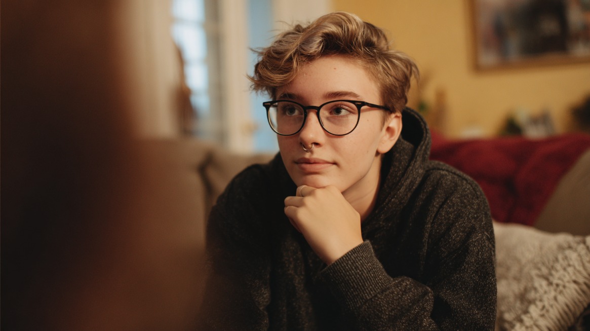 Person wearing glasses resting their chin on their hand while engaged in a conversation indoors