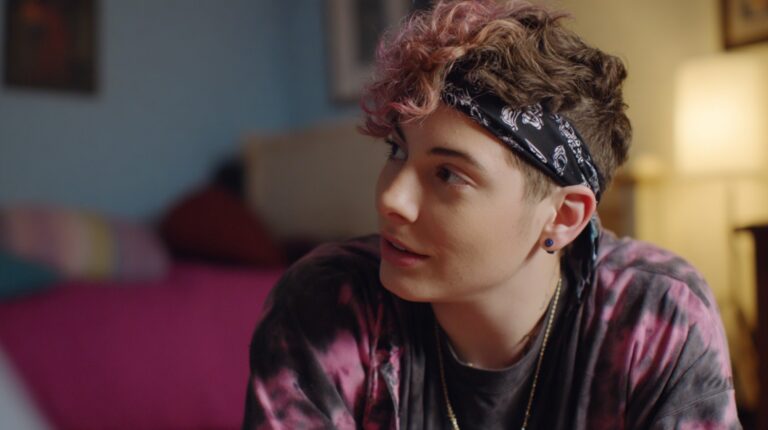 Person with short curly hair and a bandana sitting indoors, looking engaged in conversation