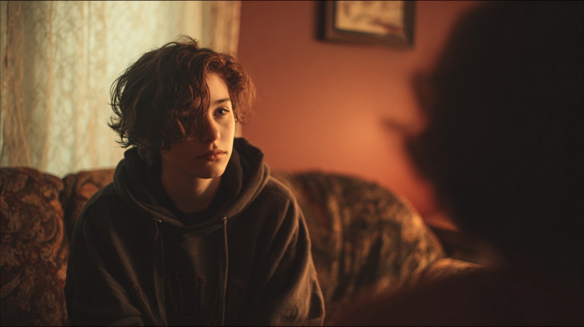 Person sitting on a couch in warm indoor light, listening thoughtfully to someone off camera